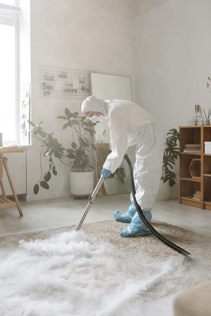 Close-up of a portable wet and dry vacuum cleaner with a clear plastic dust container filled with water and debris, connected to a flexible, patterned hose, placed on a pink carpet in a residential ro